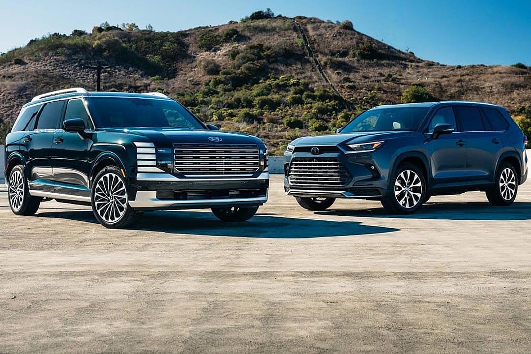 A 2026 Hyundai Palisade Calligraphy Hybrid and a 2025 Toyota Grand Highlander Hybrid parked in a concrete lot.