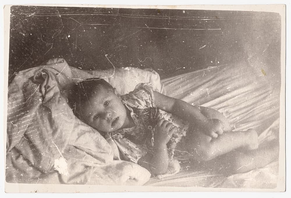 Old cute photo of a baby on a bed from the 1960s.