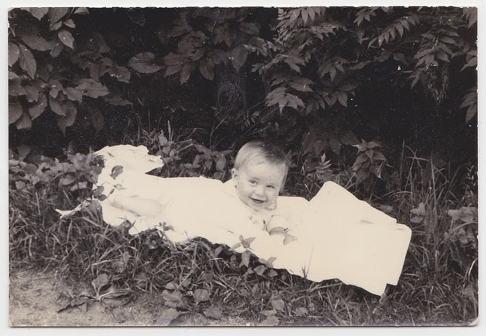 An old cute photo of a baby on a blanket in the garden. 