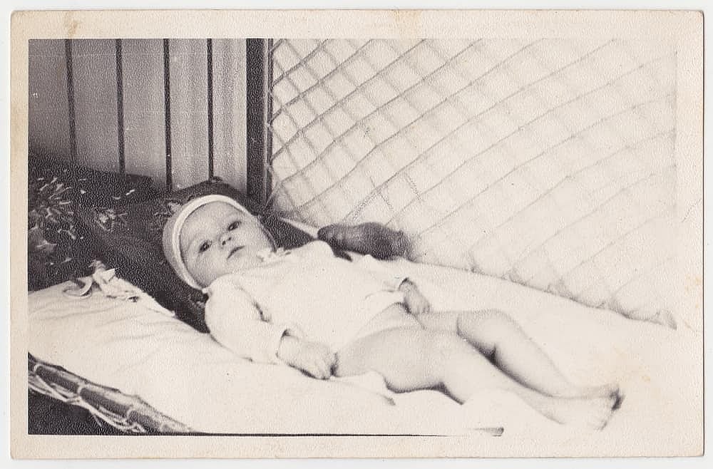 Vintage photo of a baby lying in a crib. Old, slightly yellowed with time, black and white photo taken in the USSR around 1960-1970. Photo is made on textured photo paper.