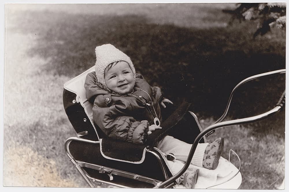 An interesting old photograph of a cute baby in a stroller. The photo has a pleasant vintage charm. This black-and-white retro shot was taken in the USSR in the 1960s.