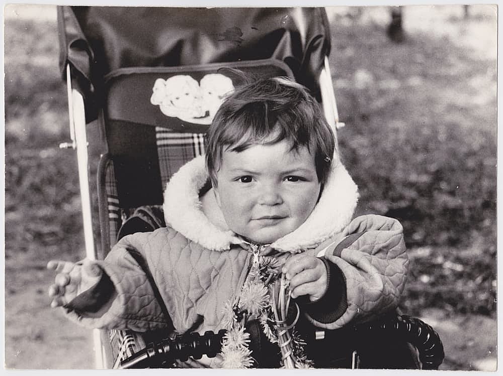 Vintage photo of a cheerful child in a stroller on the street. Old, yellowed with time black and white photo. Photo taken in the USSR around the 1960s.