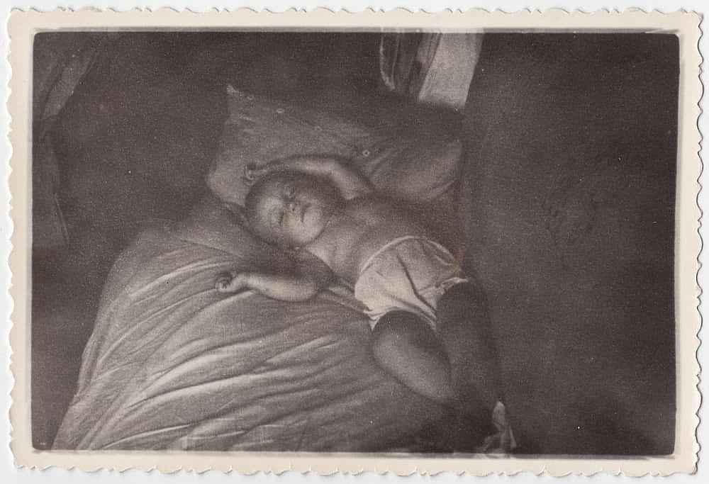 An old cute photo of a sleeping baby on a bed. Vintage black and white photo, slightly yellowed by time, taken in the USSR around 1960-1970.