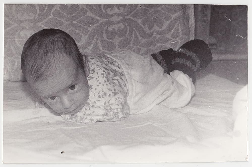 An interesting old photograph of a baby crawling on a crib. The photo has a pleasant vintage charm. This black-and-white retro shot was taken in the USSR in the 1960s.