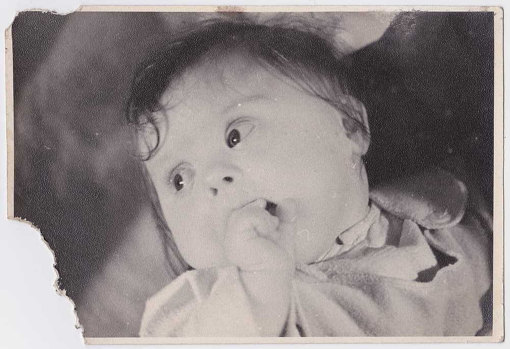 An old cute photo of a baby in an apartment. Vintage black and white photo, slightly yellowed by time, taken in the USSR around 1960-1970s.