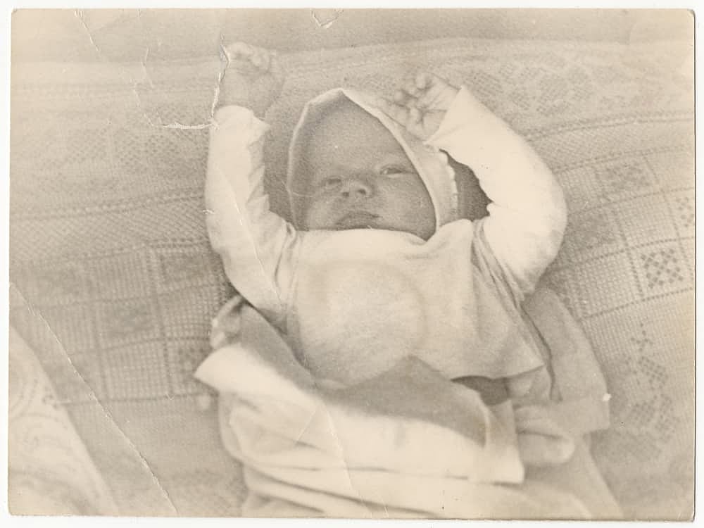 An old cute photo of a baby on a bed. Vintage, not very clear black and white photo, slightly yellowed with time, taken in the USSR around the 1960s-1970s.