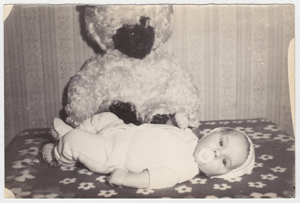 Old cute photo of a baby on a bed. Vintage black and white photo, slightly yellowed from time to time, taken in the USSR around the 1960s-1970s.