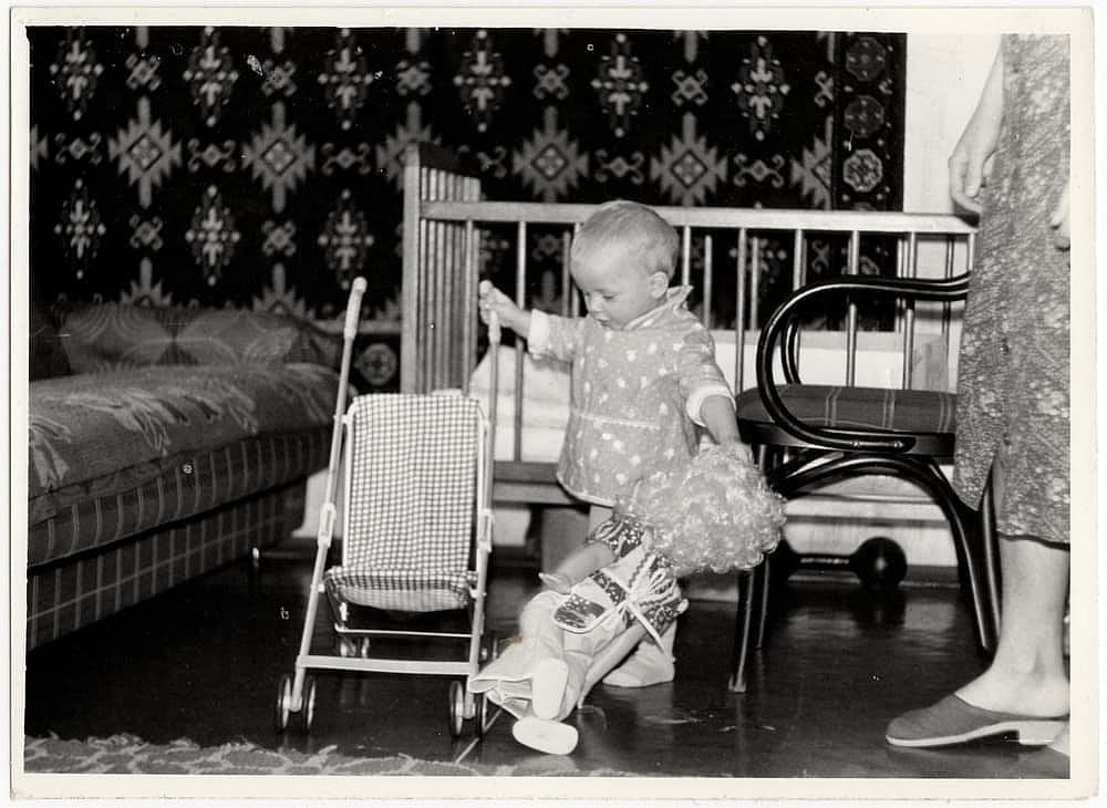 Vintage photo of a one-year-old baby with a baby carriage in an apartment in 1960.
