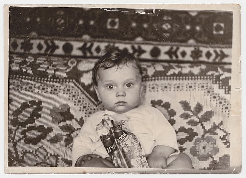 An old photograph of a baby on a sofa. This black-and-white photograph was taken in the USSR in the 1960s-1970s.