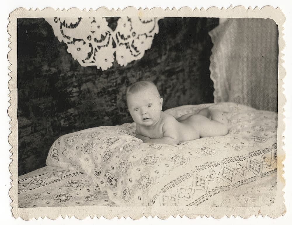 Old Black and white photographs of a young child in a baby cot.