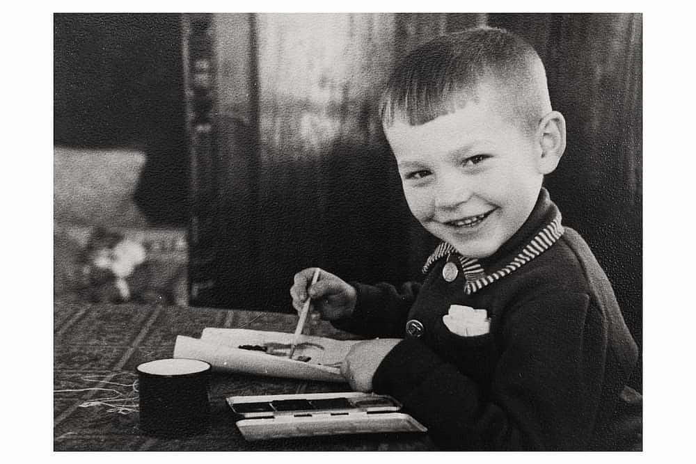 Retro portrait of smiling Soviet boy drawing with paints on paper. Vintage black and white paper photo. Early 1960s. Old surface, soft focus. Transferred property, family archive.