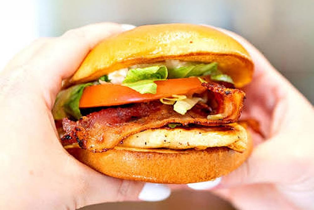 Hands holding a grilled chicken club sandwich from Bojangles