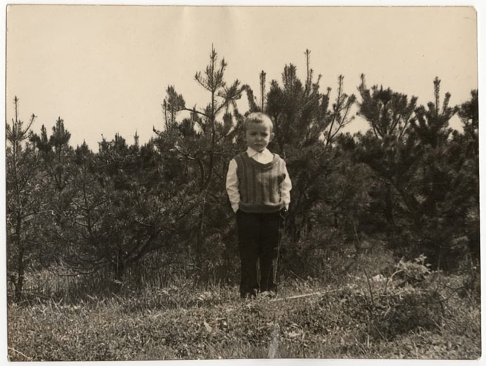 Vintage photo of a little boy against the backdrop of young pine trees. Old black and white photo taken in the USSR around the 1950s-1960s.