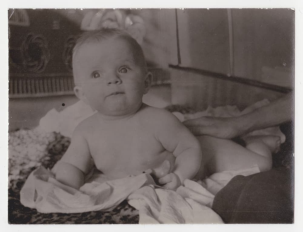 Old cute photo of a baby on a bed. Vintage black and white photo, slightly yellowed from time to time, taken in the USSR around the 1960s-1970s.