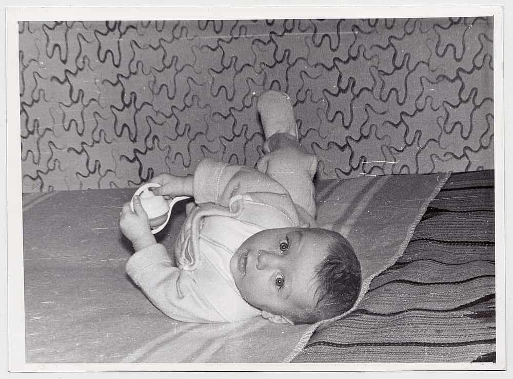 An interesting old photograph of a cute baby lying on a made bed. The photo has a pleasant vintage charm. This black-and-white retro shot was taken in the USSR in the 1960s.