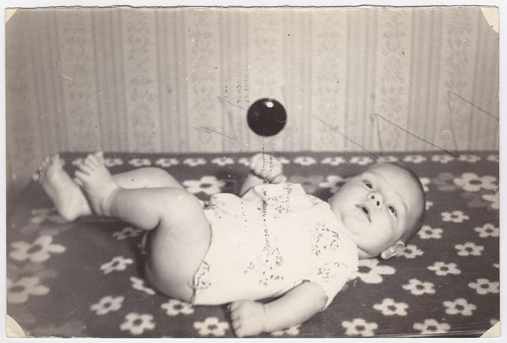 An old photograph of a cute baby on a bed. The old black-and-white photograph was taken in the USSR in the 1960s-1970s.