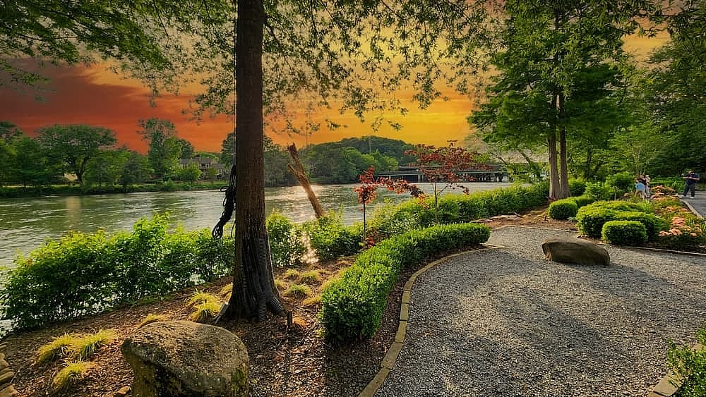 A gorgeous spring landscape along the Chattahoochee River with lush green trees, grass and plants and colorful flowers with powerful clouds at sunset at Ray’s on the River in Sandy Springs Georgia