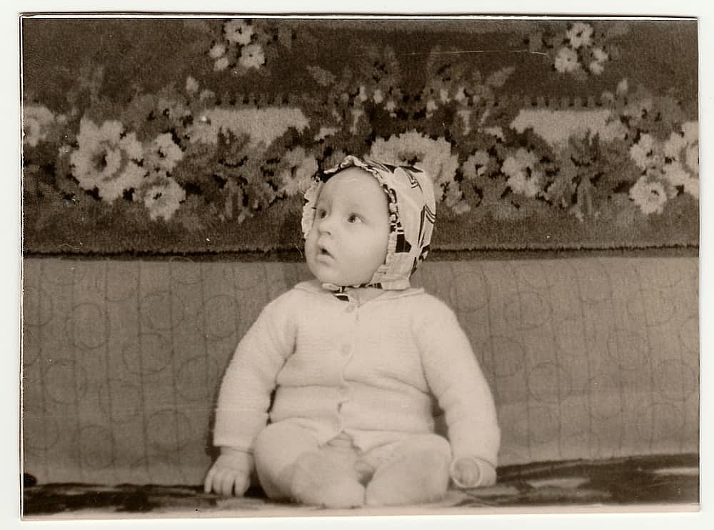 Cute baby sits on the divan. Concept of carefree childhood. Black and white antique photo. The 1960s
