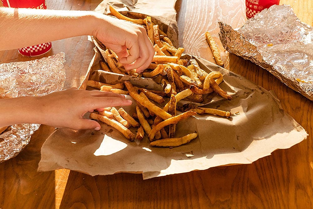 Two hands reaching into a pile of Five Guys french fries