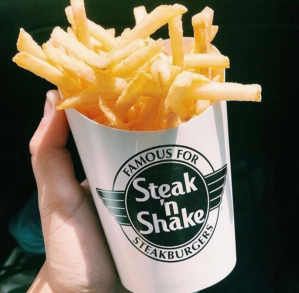 A hand holding an order of Steak 'n Shake french fries
