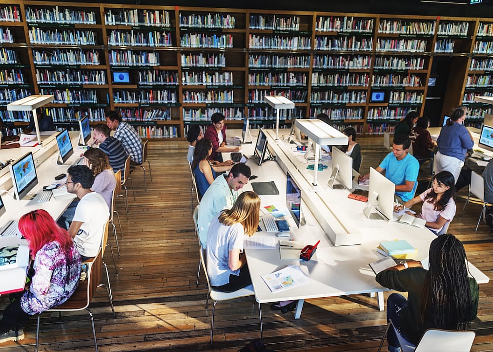Elevated view of students working at table with computers in library.