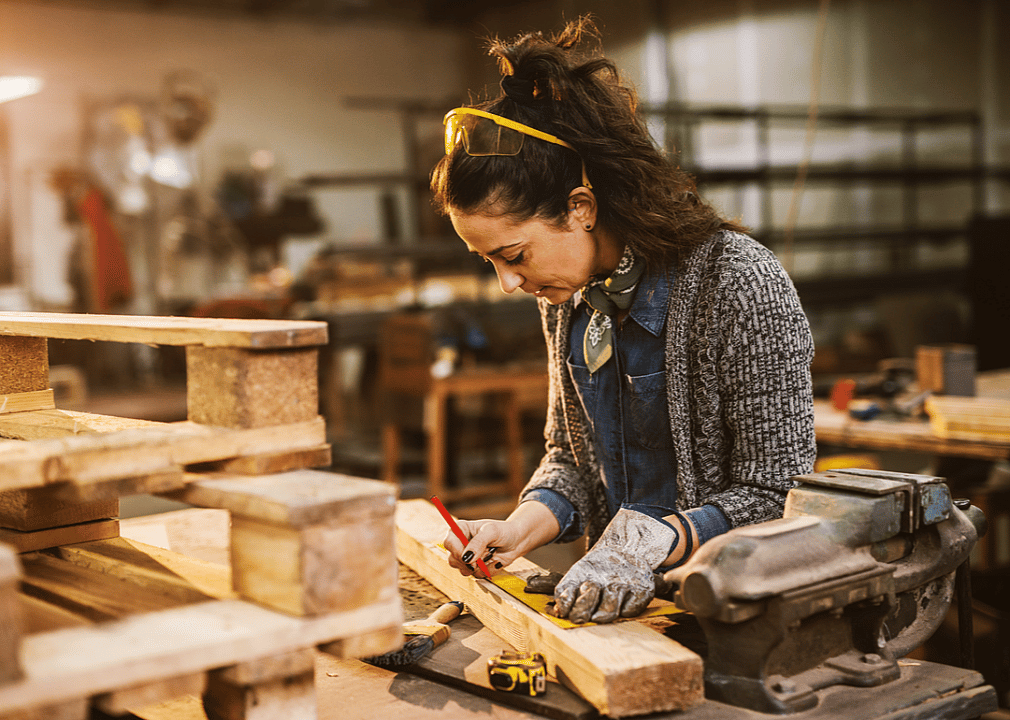 A worker makes a measurement on a piece of wood.