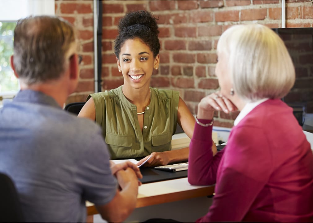 A salesperson smiles while sitting across from two clients.