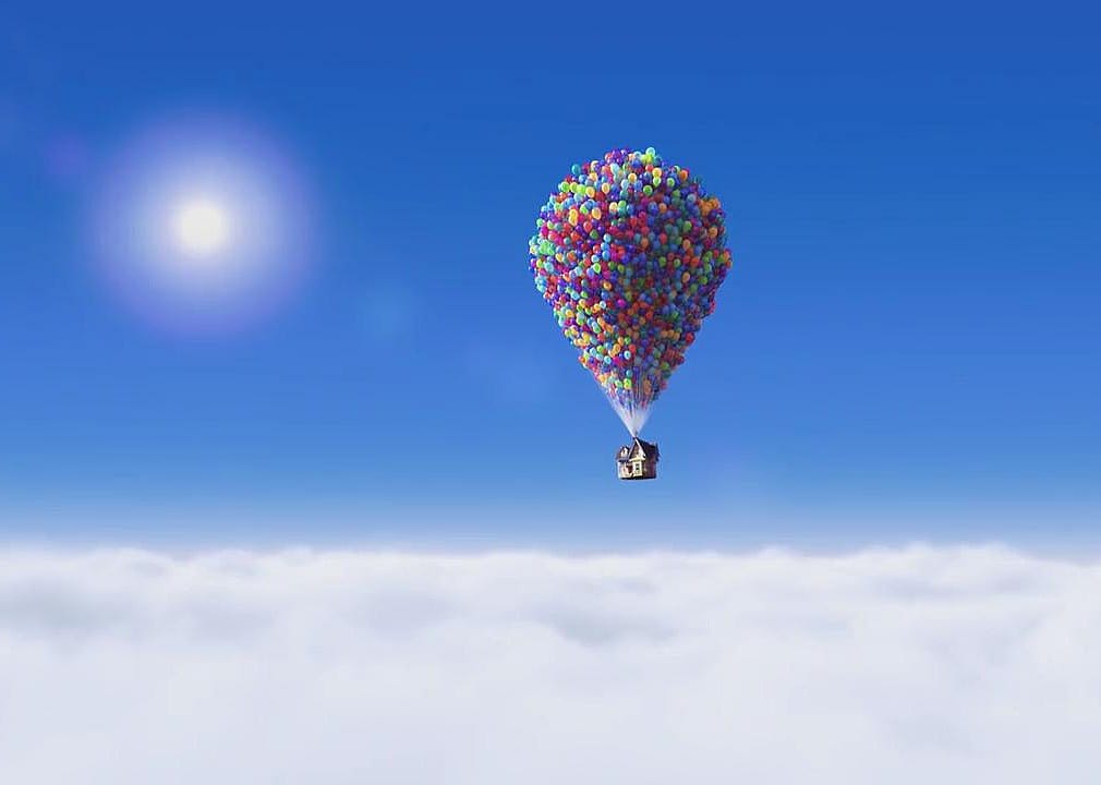 A house being held up by balloons floating through the sky.