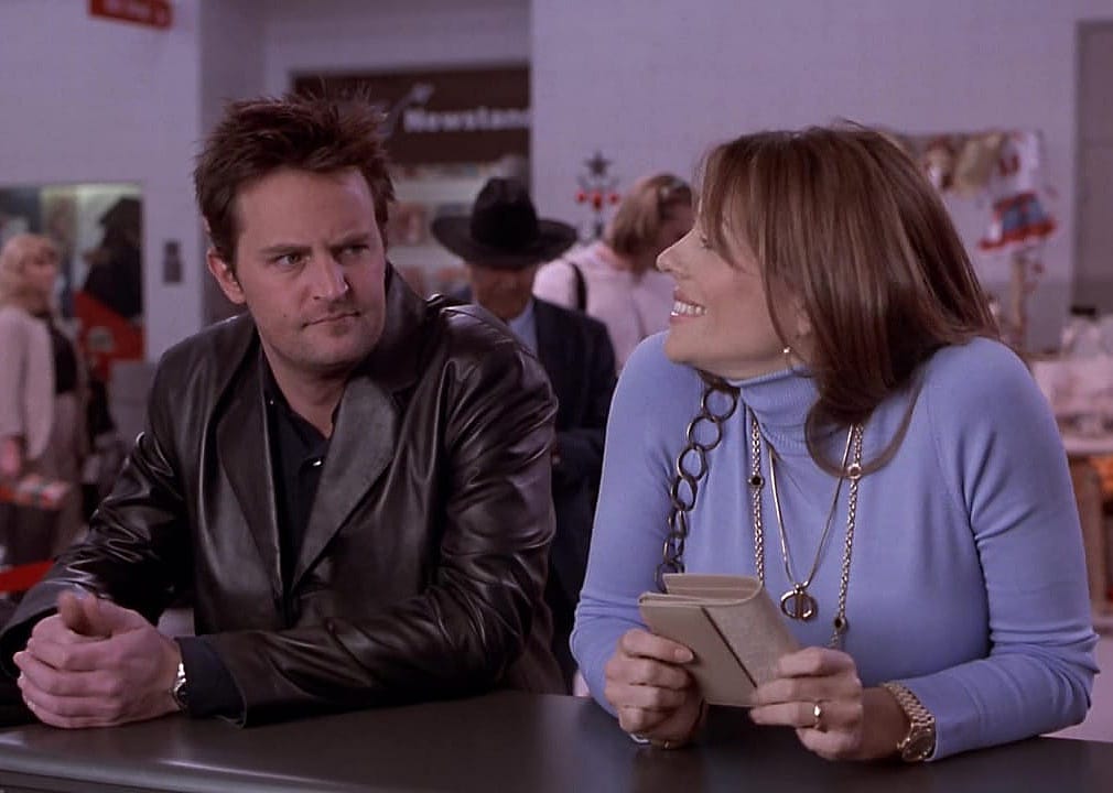 Matthew Parry sitting at a bar talking to Elizabeth Hurley, smiling.