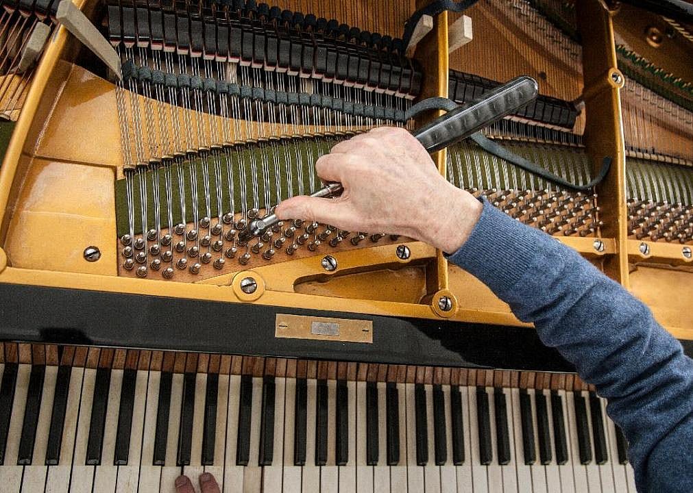 A man uses a tool to tune a piano.