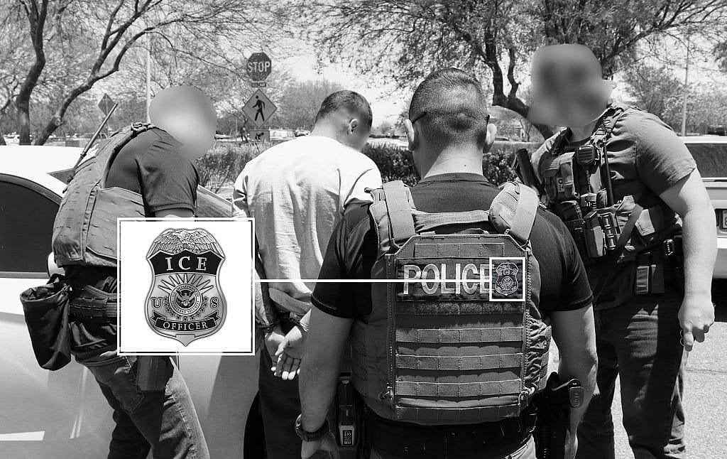 Black and white photo of  group of four U.S. Immigration and Customs Enforcement (ICE) officers, wearing tactical vests and armed with weapons, detain a man in a white shirt with his hands cuffed behind his back next to a car. Enlarged inset shows detail of ICE patch on vest.