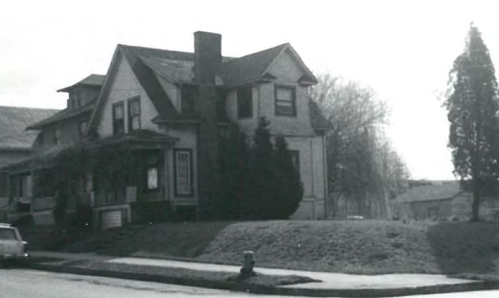 Black-and-white photo of a two-story home with a pointy roof owned by Mike Hepburn’s grandparents. 