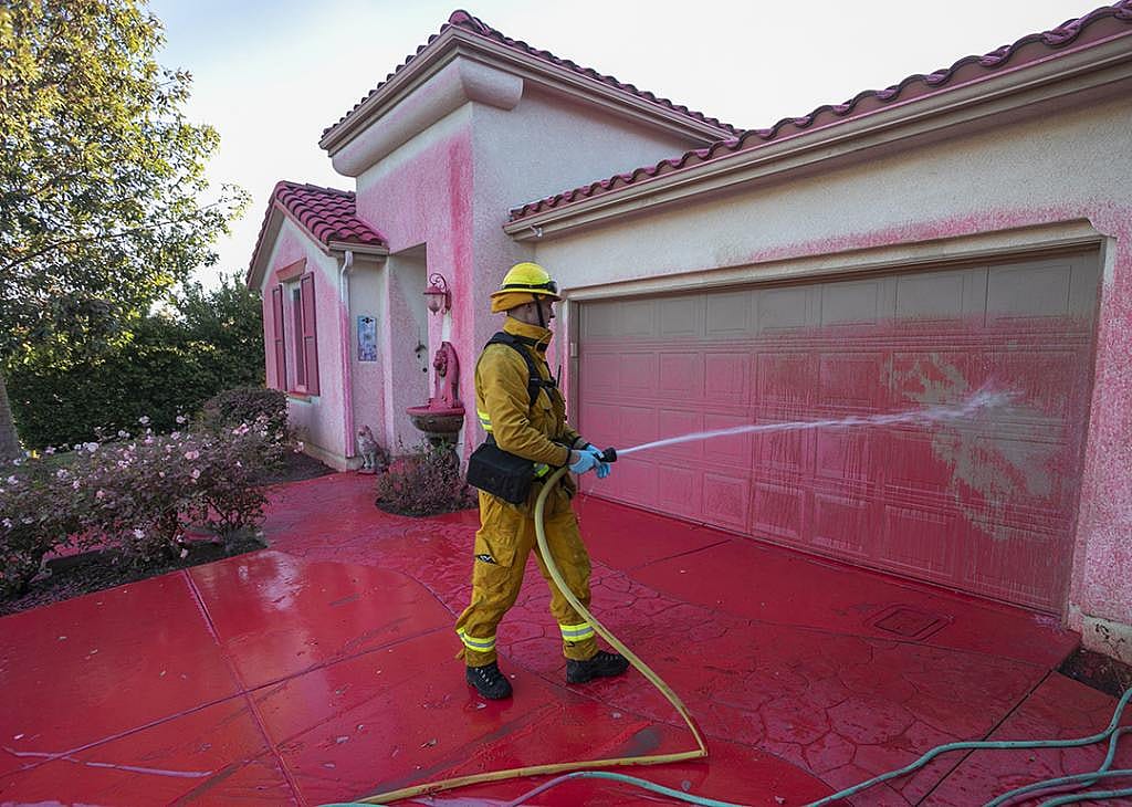 A firefighter cleans Phos-Chek fire retardant from a home.