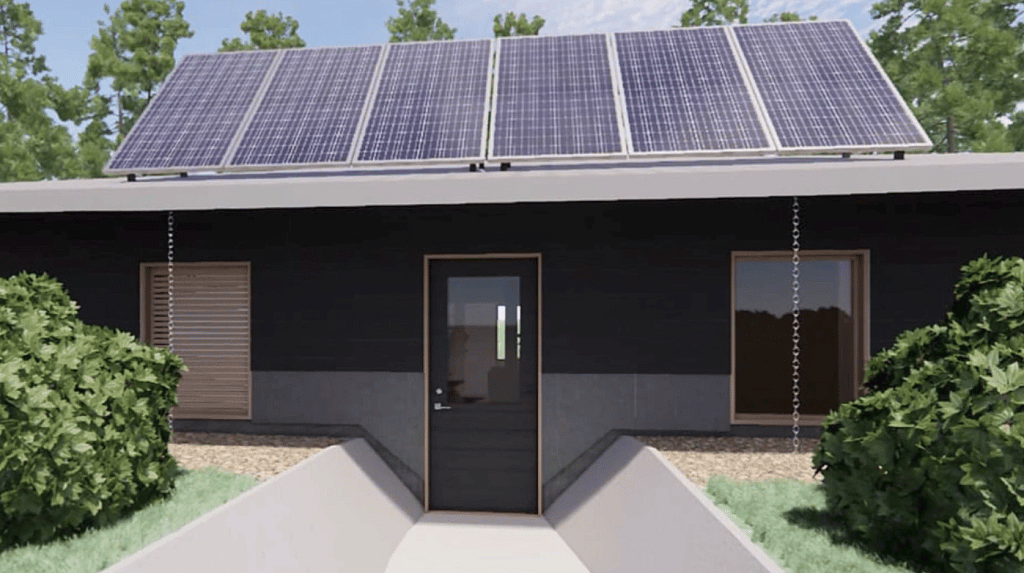 View of front door of house design worked to emulate traditional Yunesit’in pithouses, with the house partly set in the ground and a centre-point of a skylight and stove that emulates a circular home.