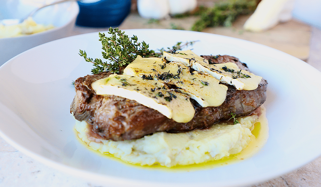 A plate of grilled New York strip steak with creamy brie.