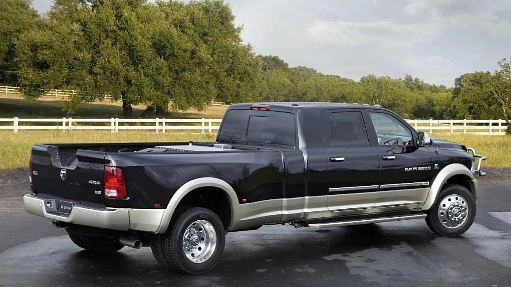 Black concept truck with extra-long truck bed parked on asphalt in front of white fence and field.