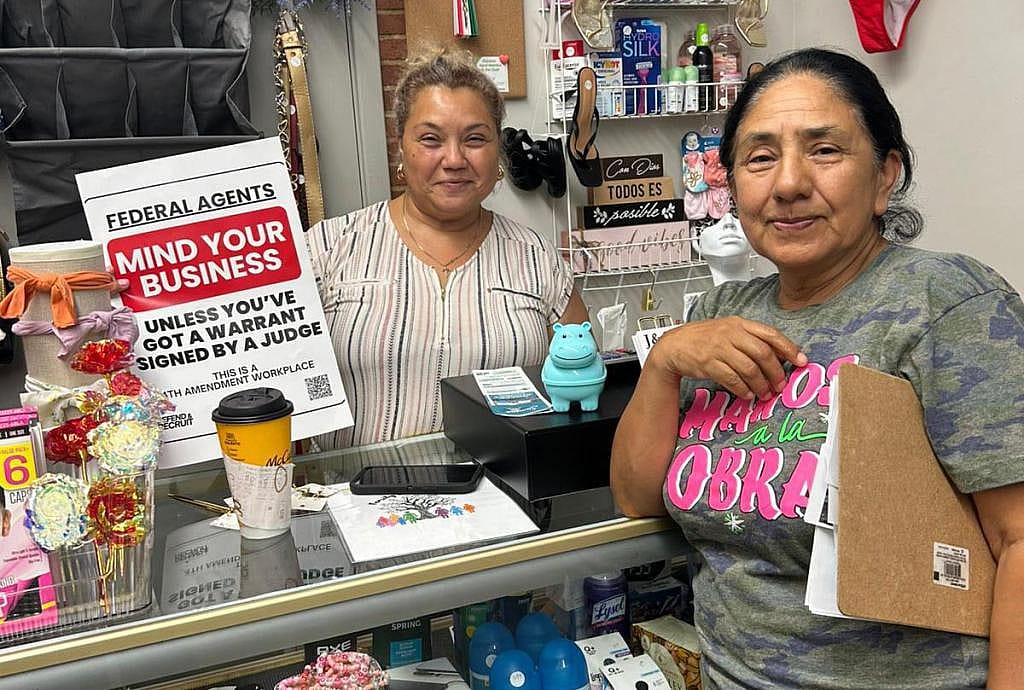Two people standing at a counter showing the 4th Amendment Workplaces signage for their business.
