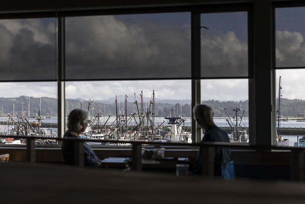 Diners inside a restaurant with a view of the ocean just outside the window.