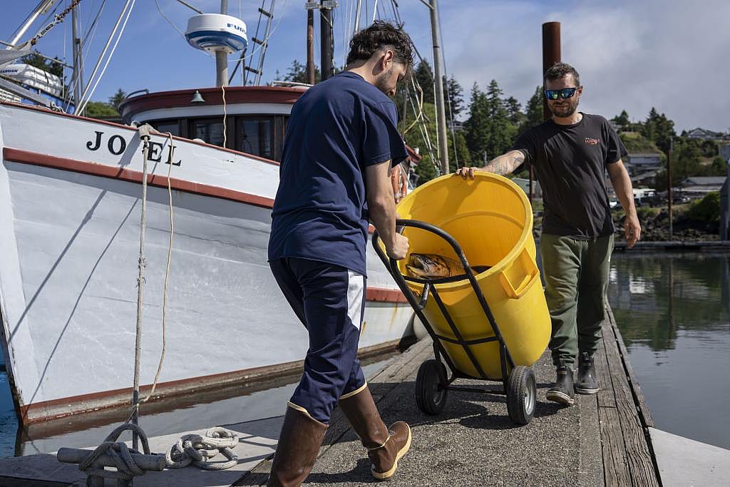 Fishermen wheeling a dolly with a large yellow bin of fish on the dock next to the boat Jo El.