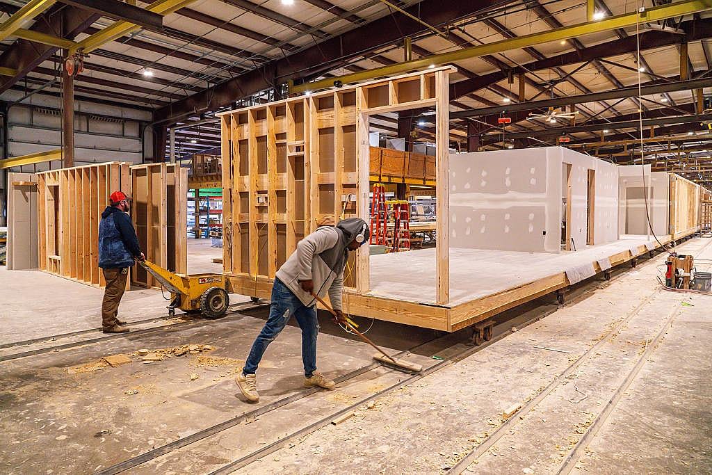 Two workers pushing a large platform on tracks that carry builds at Apex Homes, a modular housing factory in Middleburg, Pennsylvania.