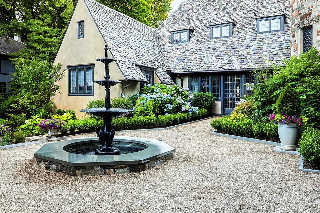 Front view of a house that has a courtyard inspired by French and Italian styles, it includes a circular space with a fountain in the middle.