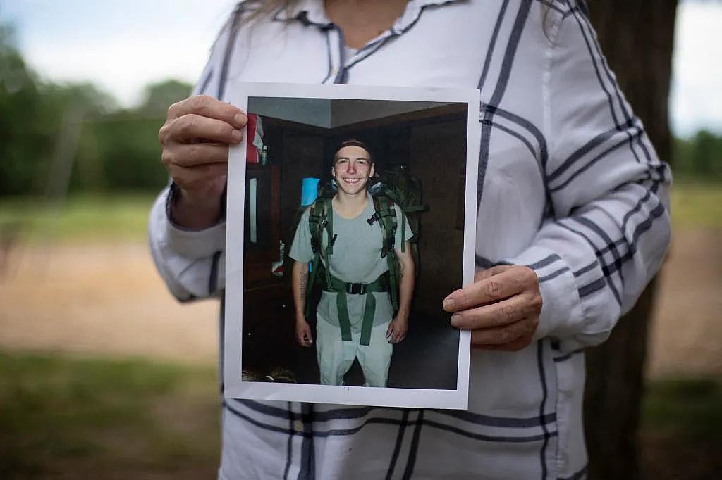 A photo of David Couch wearing a gray t-shirt, light pants and a backpacking pack smiling at the camera, the photo is in the hands of his mother Jeanelle Couch who is standing in Cascade Park in Redding on April 8, 2026.