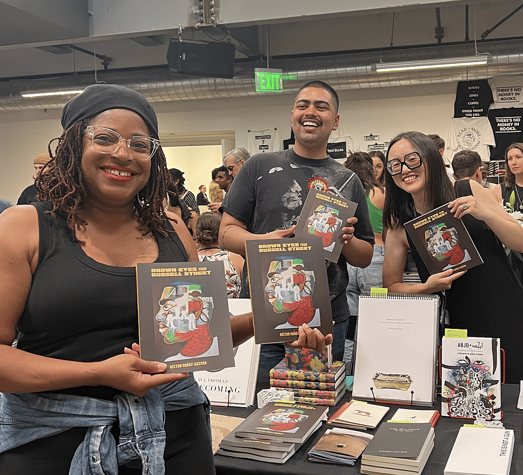 Three people holding up the book "Brown Eyes on Russell Street" at the San Francisco Art Book Fair.