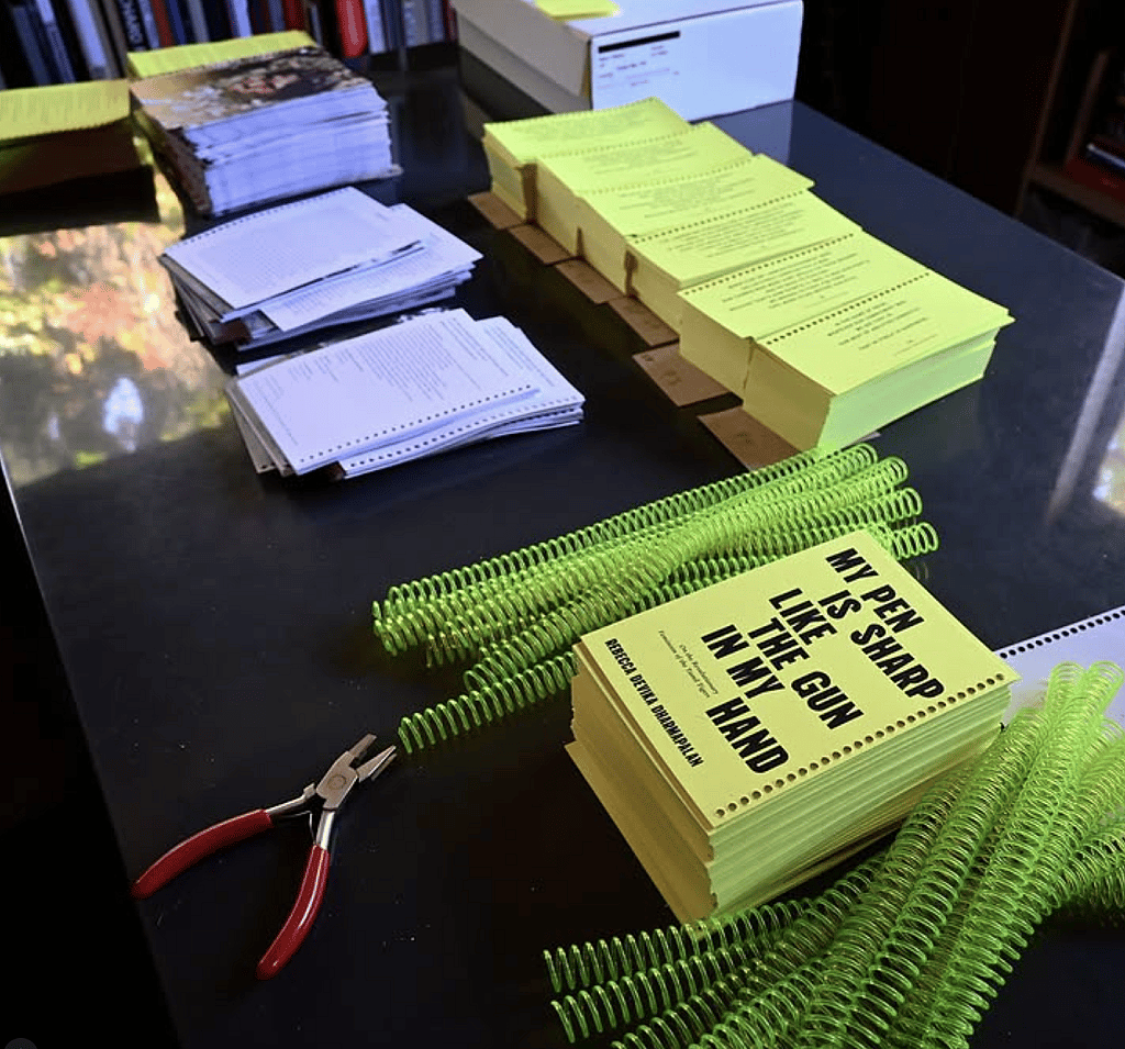 A small book called "My Pen is Sharp Like the Gun in My Hand" in the process of being bound with neon coils.