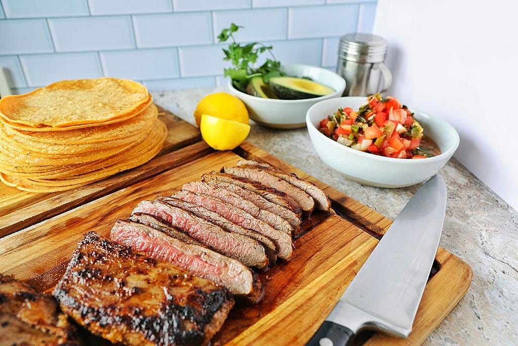 A plate of sliced carne asada with salsa and tortillas on the side.