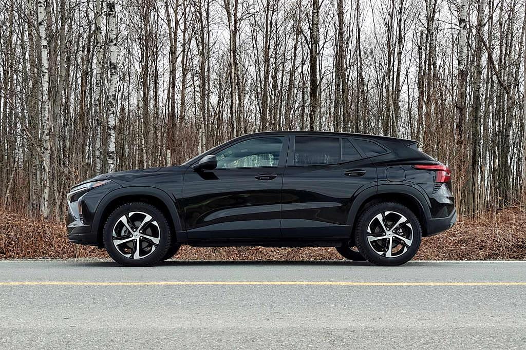 Side view of black 2026 Chevrolet Trax parked on road in front of bare trees.