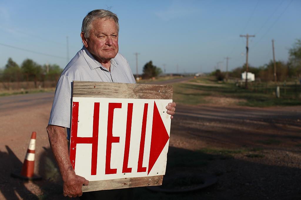 Paul Daniel, 81, who lives directly beside OpenAI’s Stargate data center, said he was never informed of the project until it was too late to leave. He holds a homemade sign with red letters spelling "HELL" with an arrow that he has placed on the road leading to Stargate’s entrance.