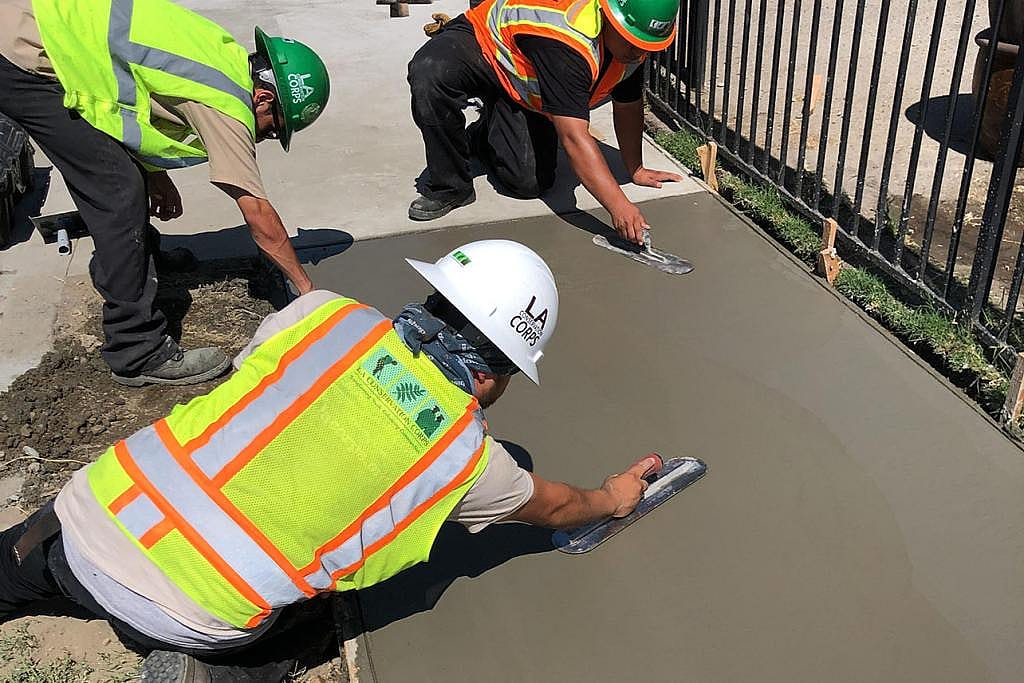 Three members of the LA Conservation corps finishing a sidewalk by smoothing the concrete it from different sides.