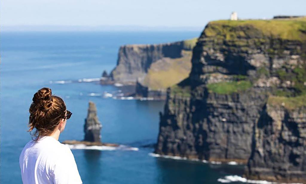 A female tourist looking at the cliffs of Moher in Ireland.