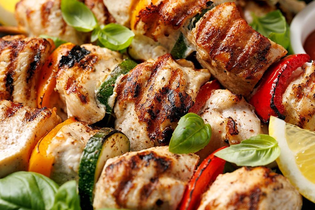 Lemon herb chicken skewers with zucchini, bell peppers, red onions, and basil leaves served in a plating dish.